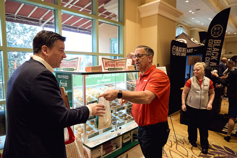 Man handing another man a Krispy Kreme doughnut